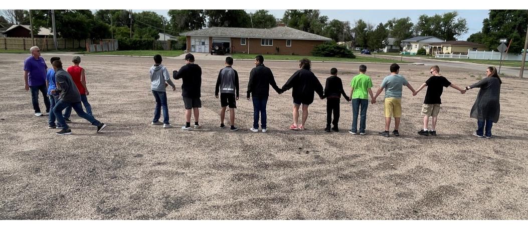 About a dozen students and two teachers; standing in a line and holding hands