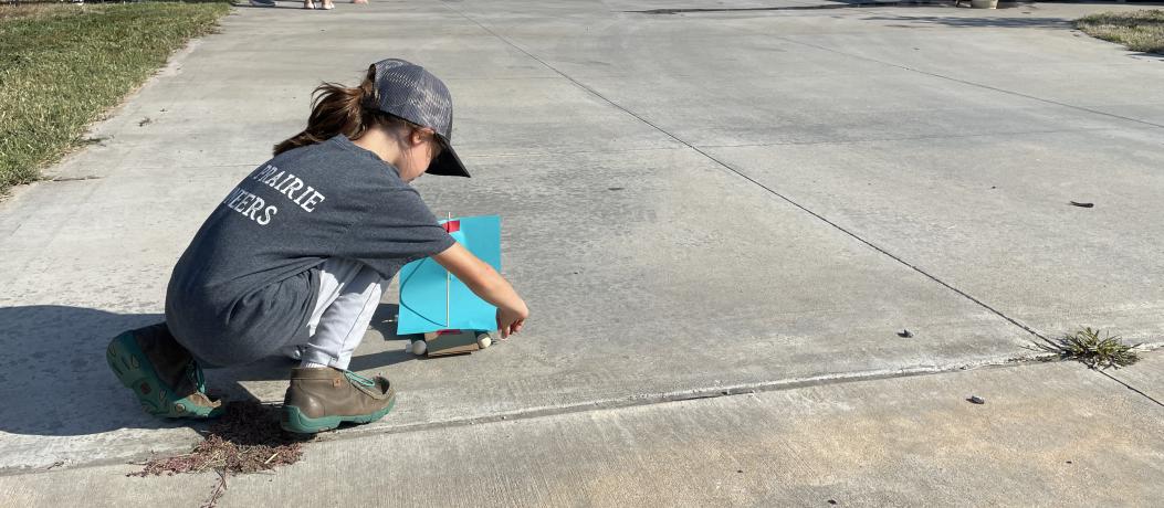 Girl facing away from camera setting her wind-powered sailcar on the concrete.