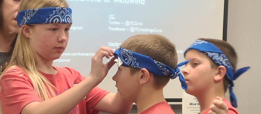 Three students helping each other put on blue bandanas as headbands