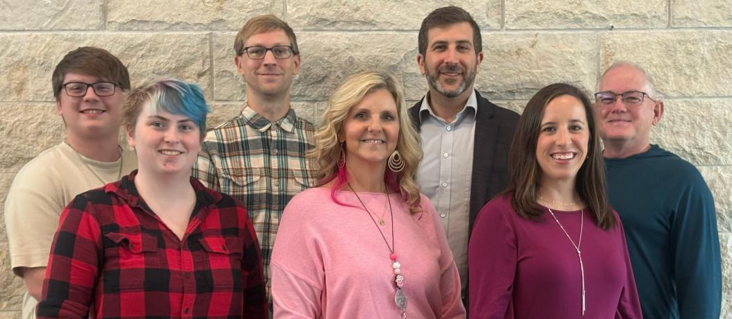 Seven people standing next to each other in front of limestone wall