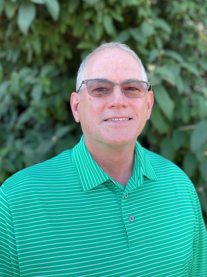 Close-up of man wearing glasses and a green shirt. Leaves and greenery in background.